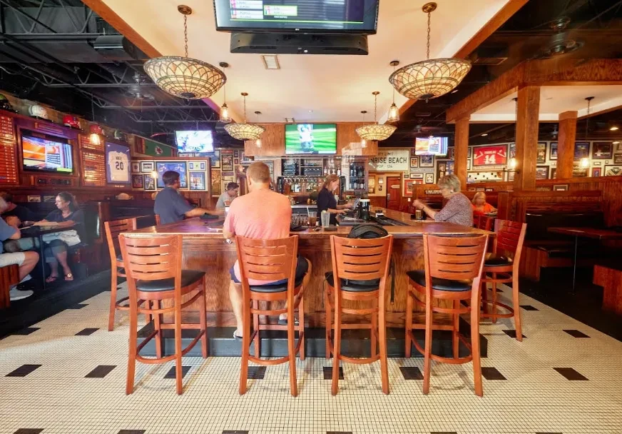 Lively sports bar interior with patrons at a wooden bar and booths.