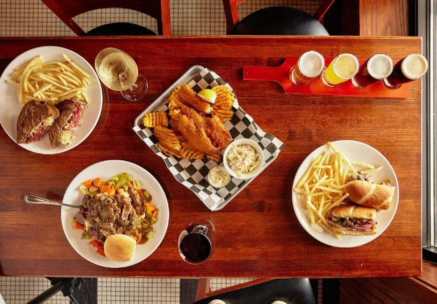 Wooden table laden with various pub dishes, a beer flight, and wines.