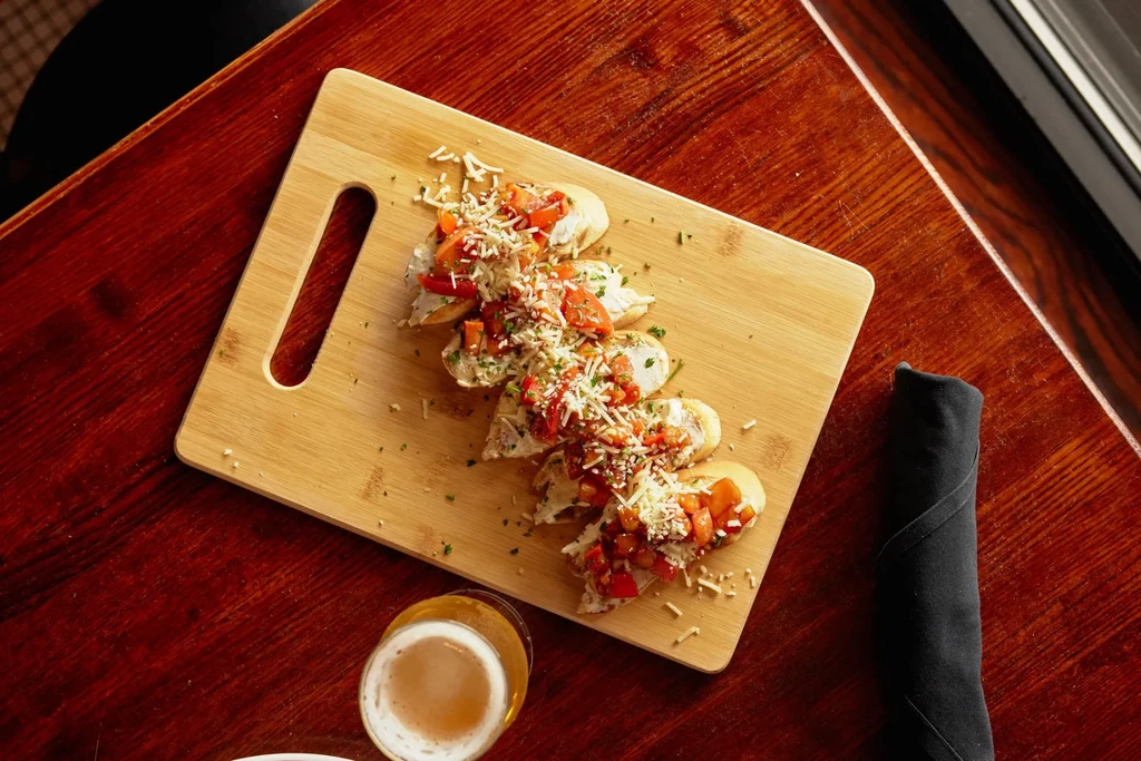 Top-down: Bruschetta appetizers and beer on a dark wooden table.