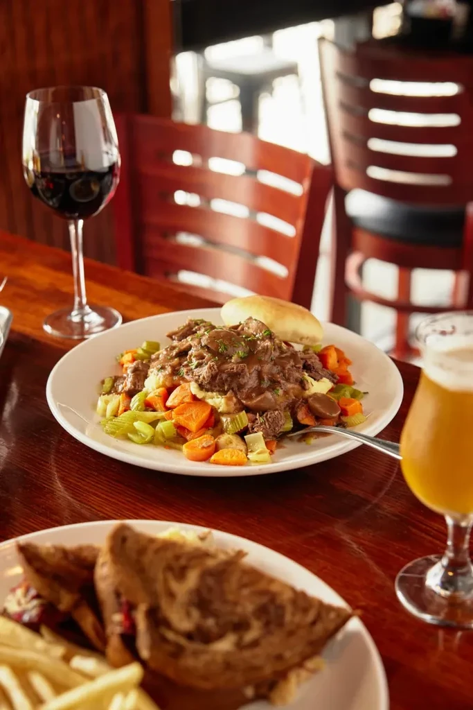 Close-up of a restaurant table with stew, sandwich, wine, and beer.