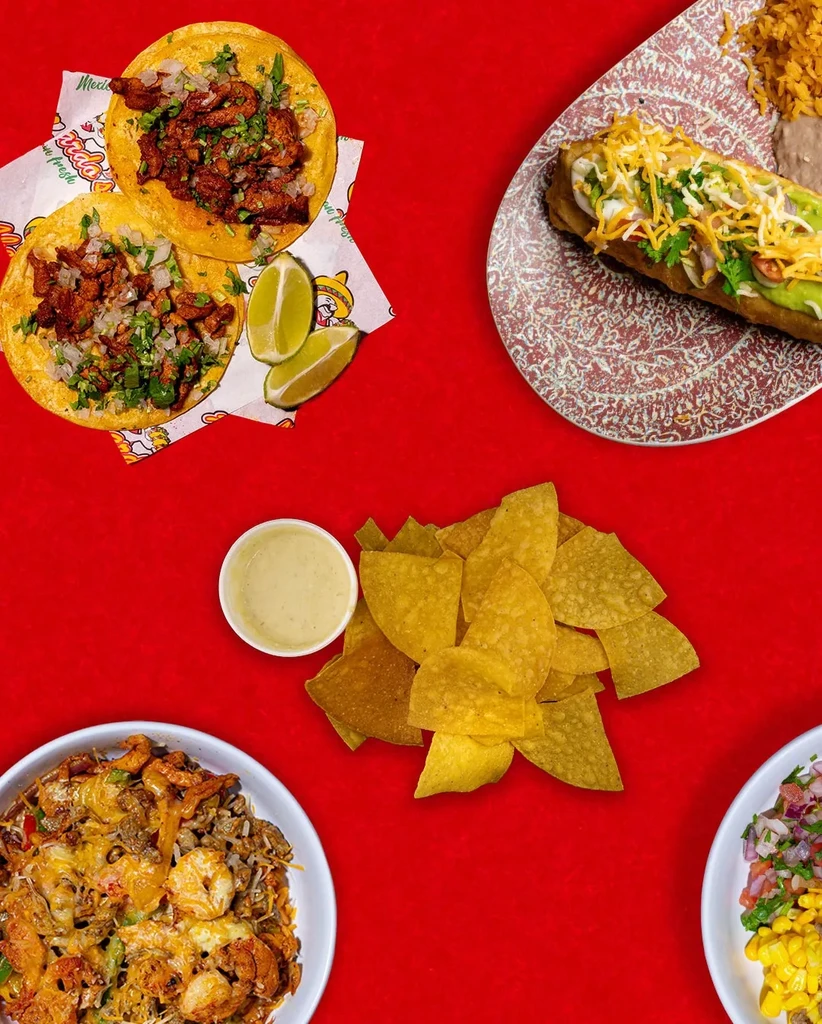 Flat lay of colorful Mexican dishes: tacos, chips, rice, and queso.