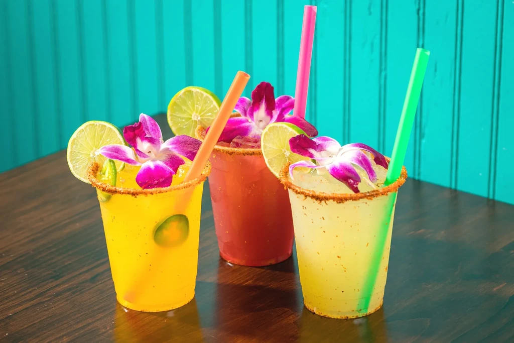 Three colorful cocktails with spiced rims, lime, and orchid garnishes.