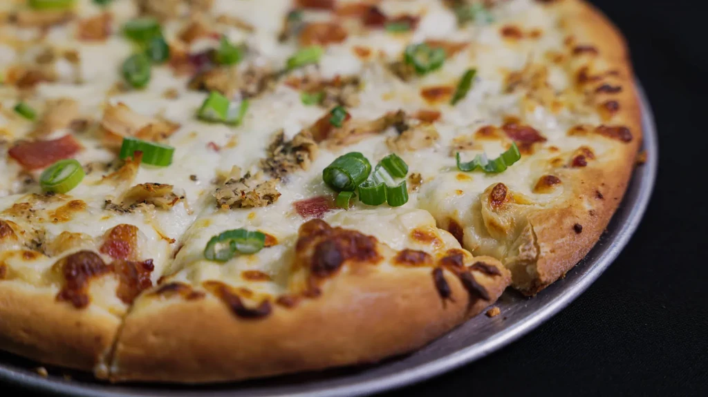 Close-up of pizza with chicken, cheese, bacon, and green onions.