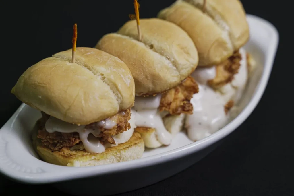 Four crispy fried chicken sliders with creamy sauce in a white dish.