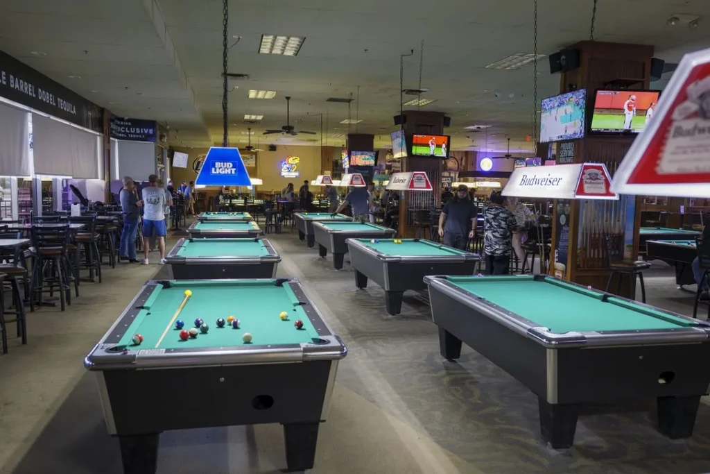 A large, lively pool hall with many tables and active patrons.