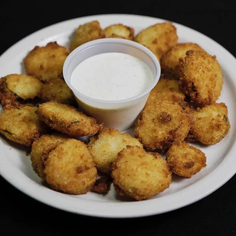 White plate of golden-brown fried pickles or zucchini with creamy dip.