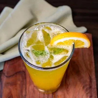 Tall glass of yellow-orange drink with ice, mint, and orange.