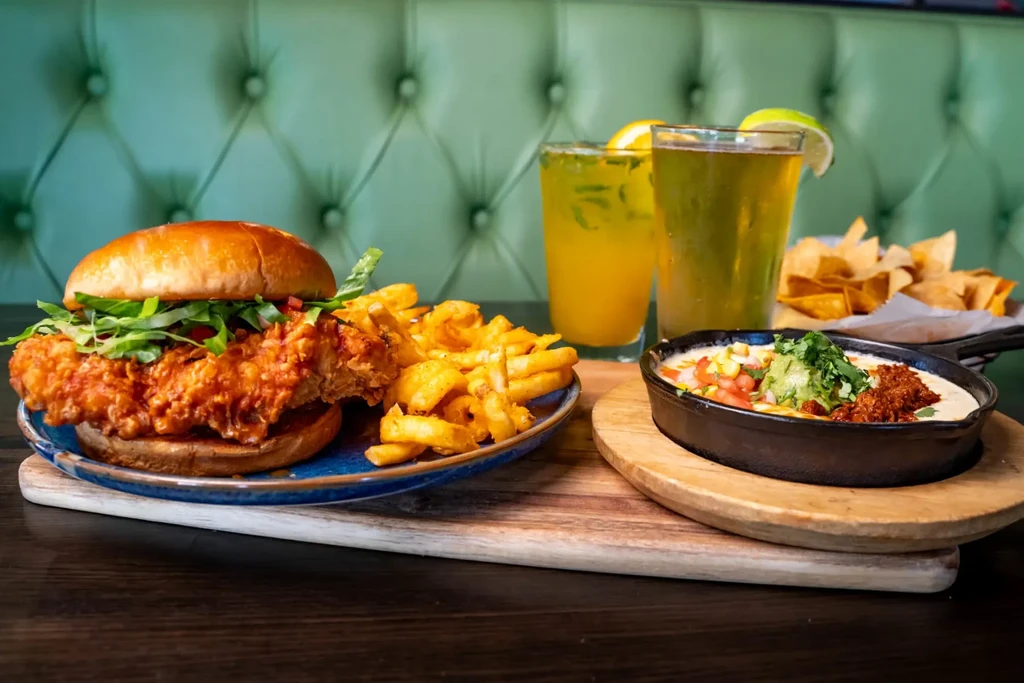 Fried chicken sandwich, fries, queso dip, and beverages on a restaurant table.