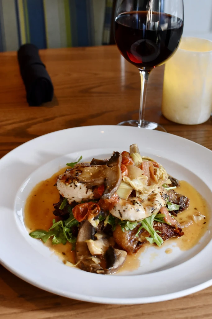 Gourmet chicken or fish dish with mushrooms, tomatoes, wine, and candle.
