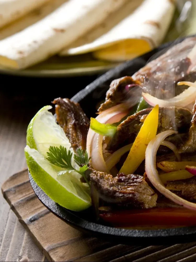 Sizzling fajitas with meat, peppers, onions, lime, and tortillas.