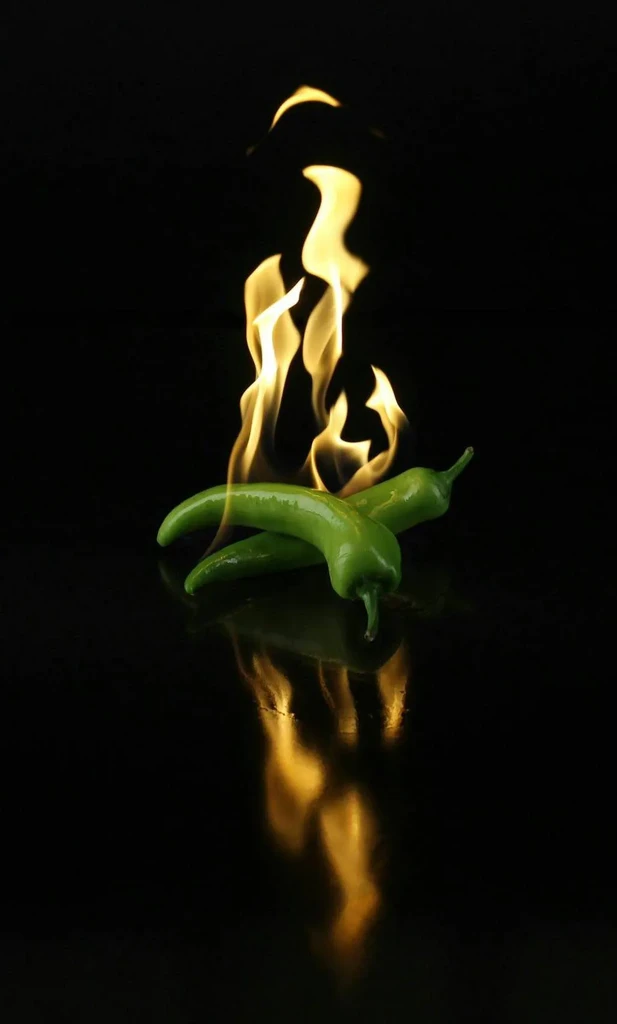 Two green chili peppers with vivid orange flames and reflections.