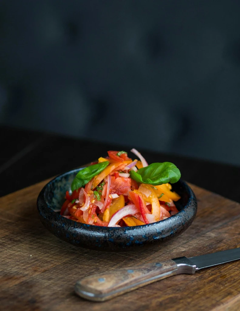 Vibrant salad in dark bowl on wooden board with knife.