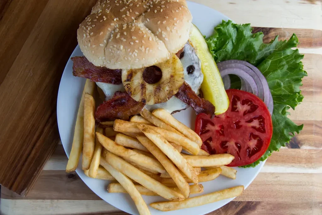 Hawaiian burger with pineapple, bacon, cheese, fries, and garnish.
