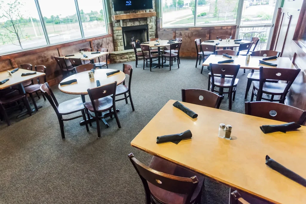 Empty rustic restaurant dining room with wooden tables and stone fireplace.