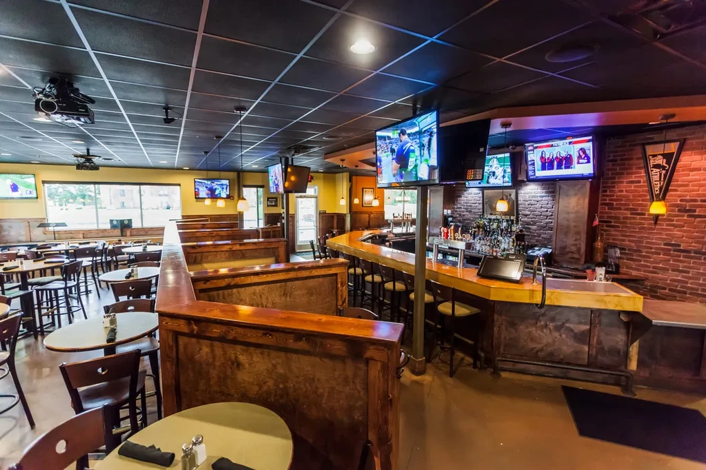 Contemporary sports bar interior: dining tables, bar, and TVs showing games.
