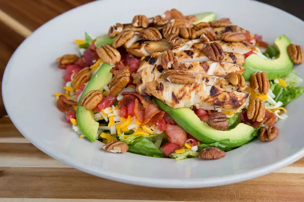 Hearty salad bowl with grilled chicken, avocado, pecans, bacon, and cheese.