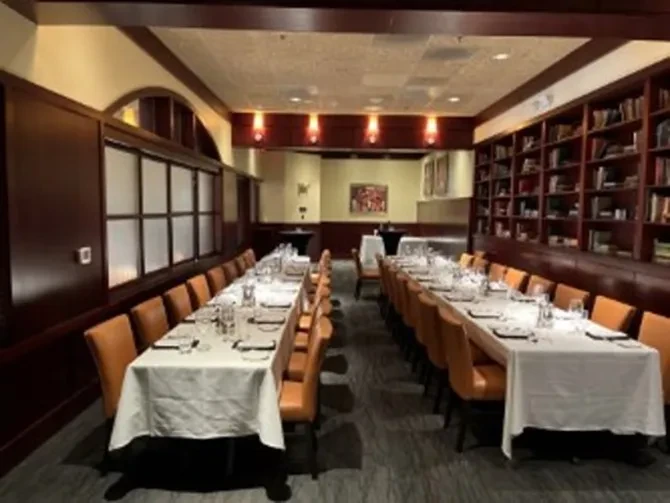 Library-style dining room with long set tables and leather chairs.