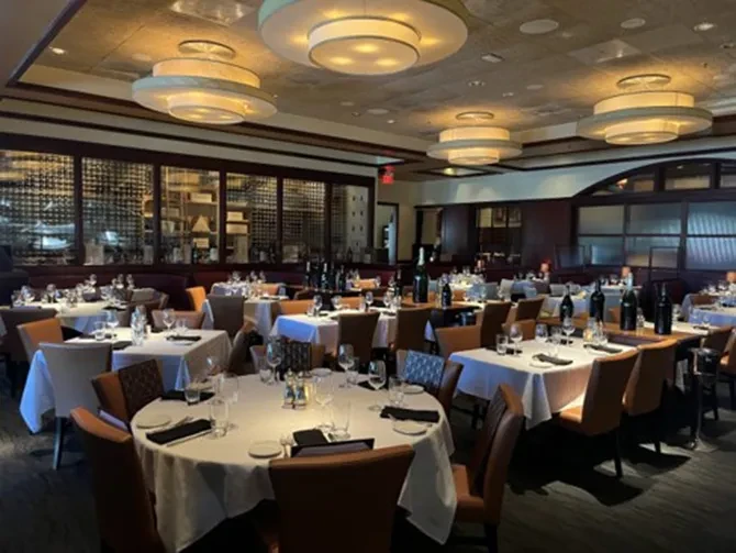 Empty, well-appointed restaurant dining room with set tables and wine rack.