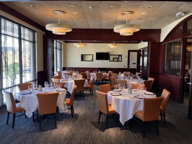 An empty, well-lit restaurant dining room with set tables and warm decor.