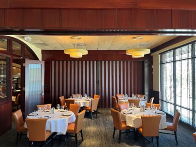Empty upscale dining room, dark wood walls, set tables, orange chairs.