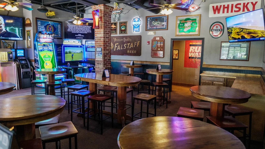 Empty sports bar interior with high tables, multiple TVs, and arcade games.