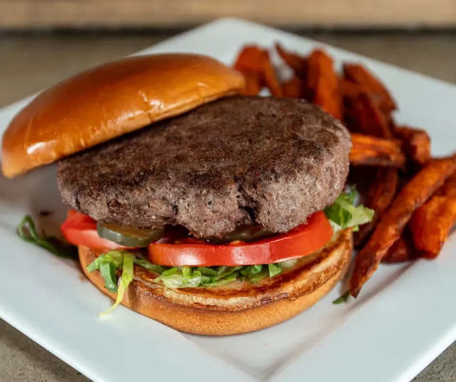 Deconstructed beef burger with lettuce, tomato, pickles, and sweet potato fries.