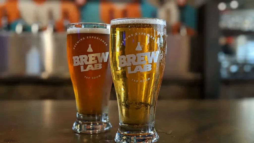 Golden lager and amber ale in branded glasses on a bar.