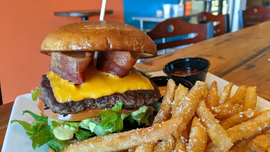 Close-up of a burger with bacon, cheddar, lettuce, and parmesan fries.