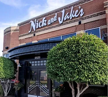 Nick and Jake's restaurant, brick exterior with white sign and green bushes.