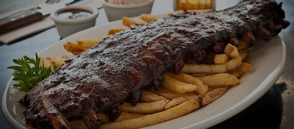 A plate of glossy barbecued ribs, french fries, and green garnish.