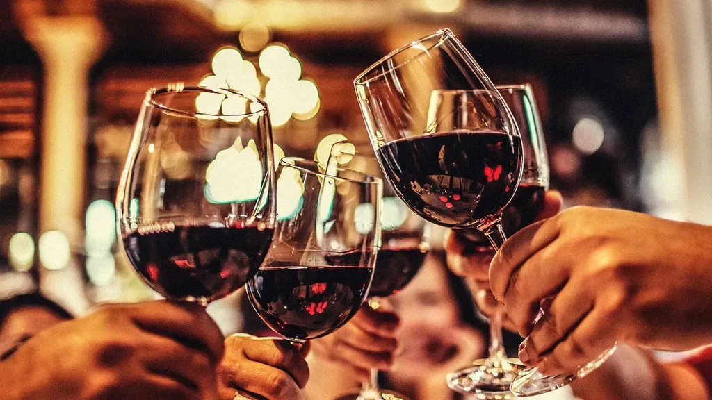 Close-up of hands clinking red wine glasses against a warm, blurred background.