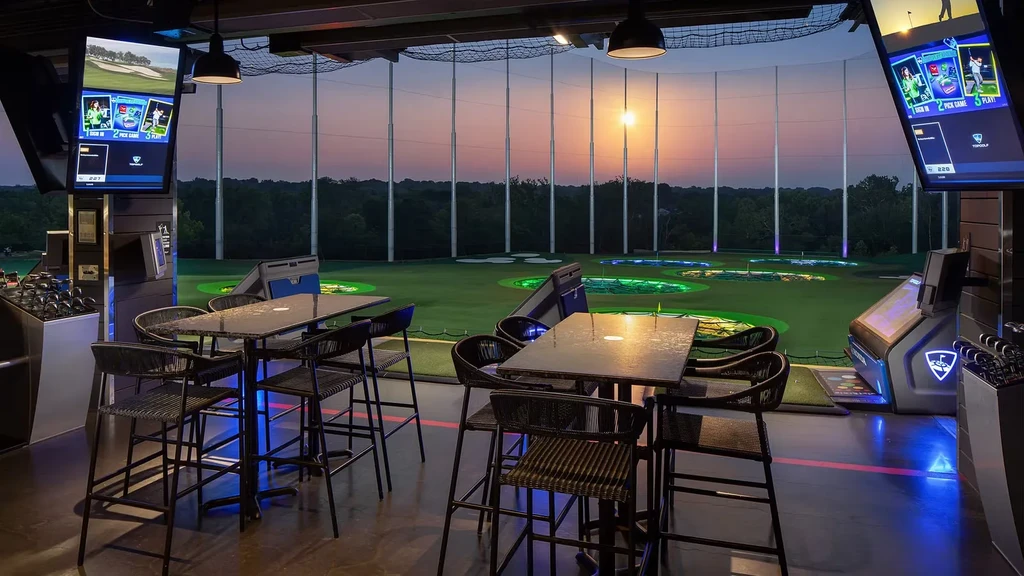 Topgolf driving range bay at dusk with screens and illuminated targets.