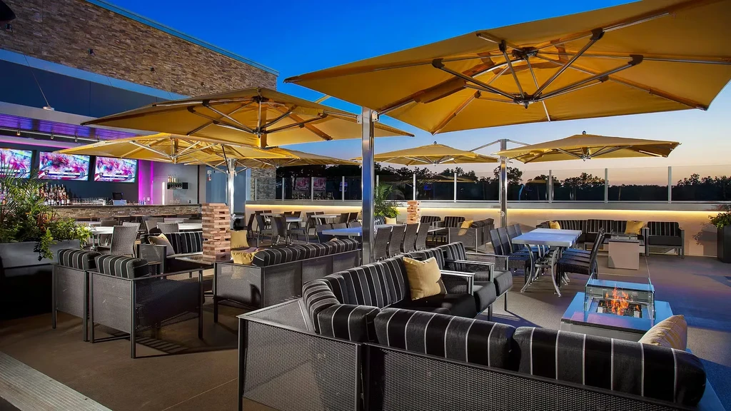 Modern outdoor restaurant patio with yellow umbrellas, bar, and fire pit.
