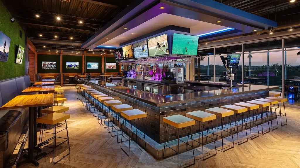 Spacious modern bar interior with blue-lit counter and multiple TVs.