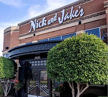 Brick exterior of Nick and Jake's restaurant entrance with large shrubs.