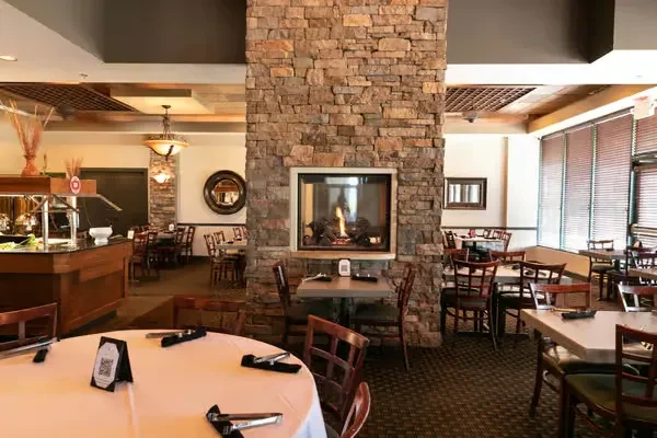 Warm restaurant interior with fireplace, set dining tables, and buffet.