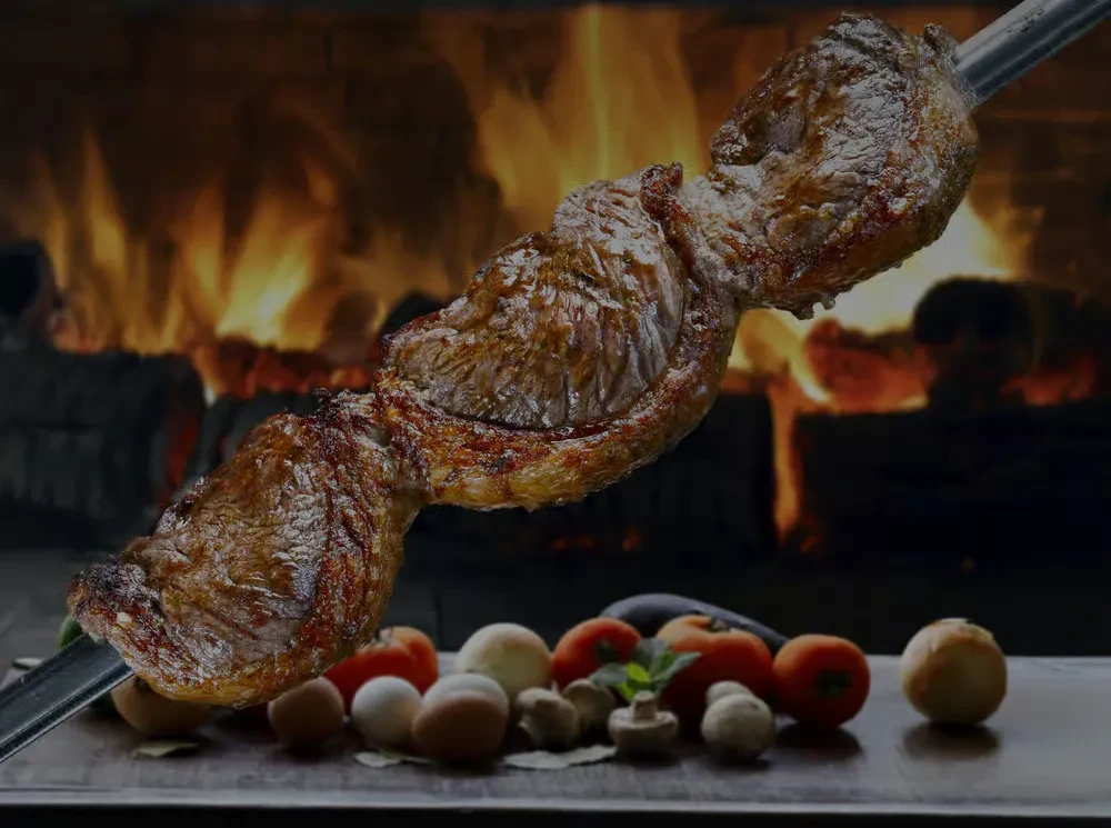 Skewered roast beef, vegetables, and eggs cooking over open flames.