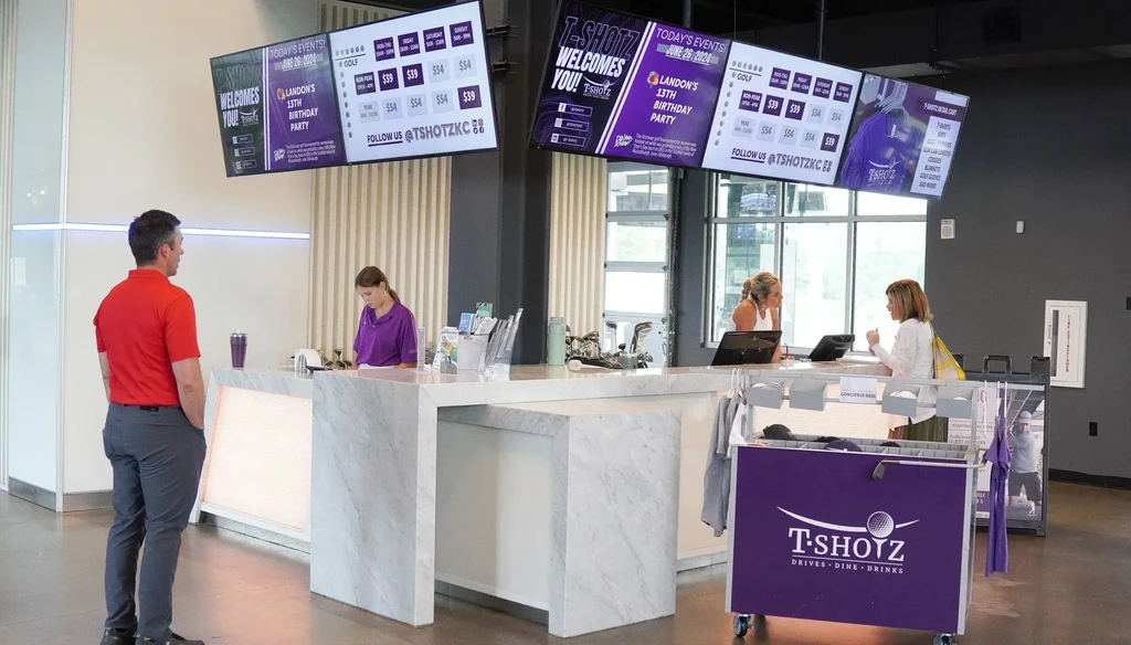 Modern T-SHOTZ interior with a long counter, digital screens, and people.