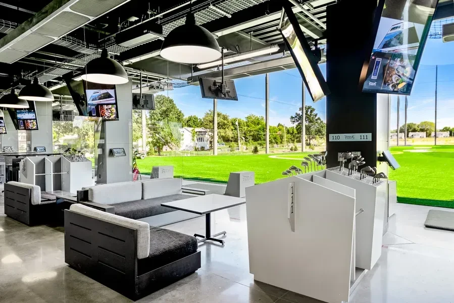 Modern golf lounge with screens, seating, and view of outdoor course.