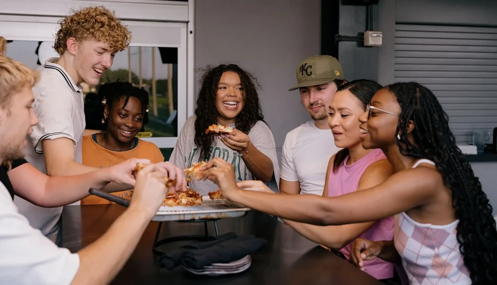 Group of young adults laughing, sharing pizza in a modern venue.