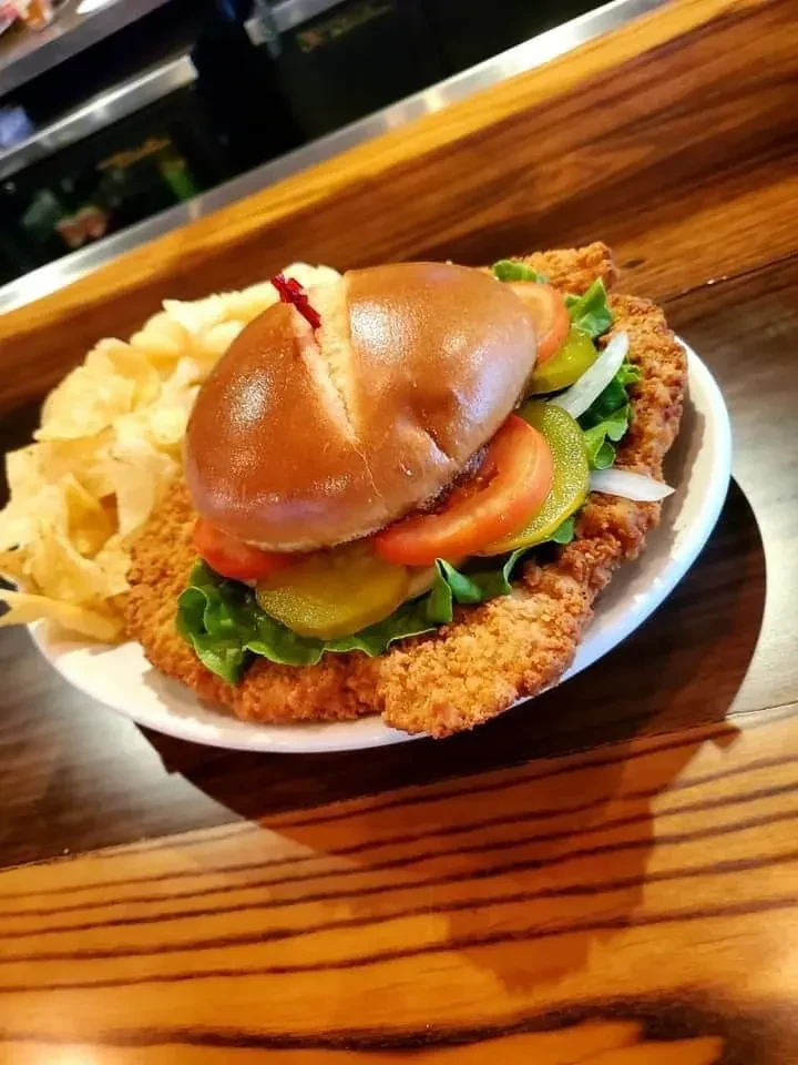 Large breaded cutlet sandwich with chips on a wooden table.