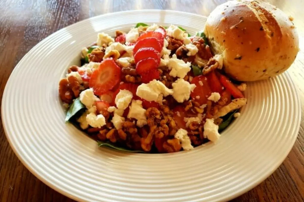 Colorful salad with strawberries, crumbled cheese, walnuts, and bread.