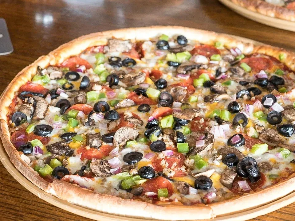 Whole pizza with pepperoni, veggies, melted cheese on a wooden peel.