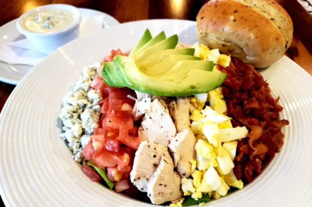 Colorful Cobb salad in a white bowl with bread and dressing.