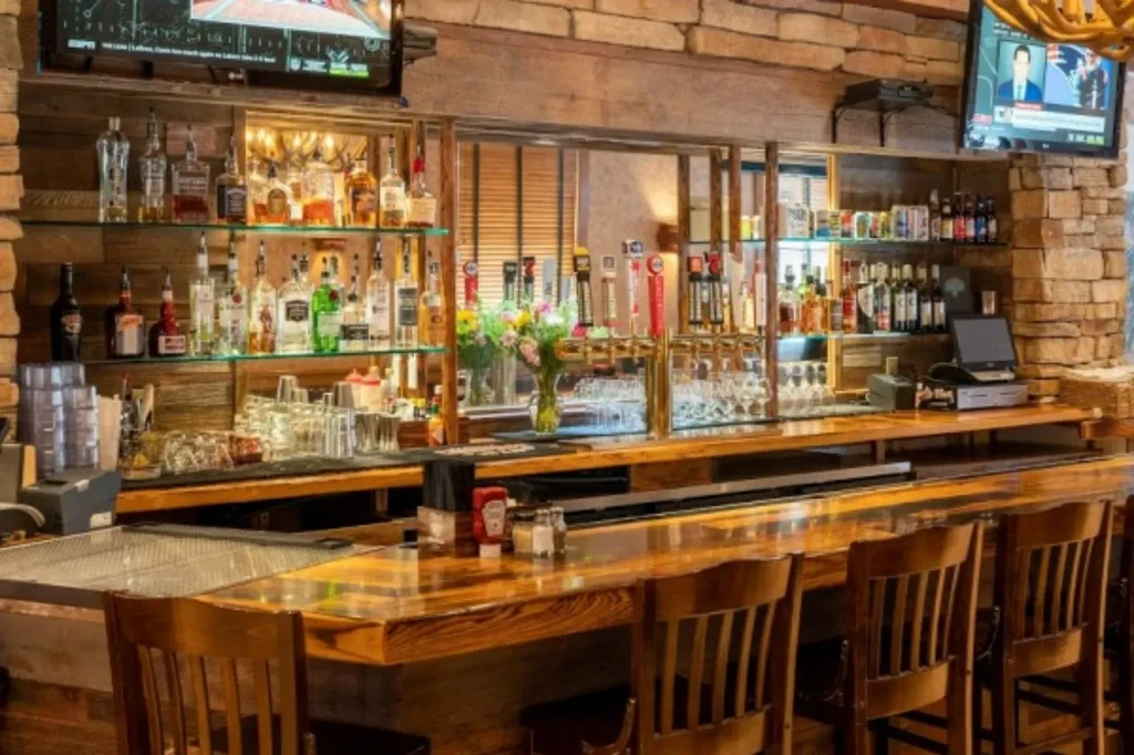 Warm rustic bar with polished wood, liquor display, beer taps, and TVs.