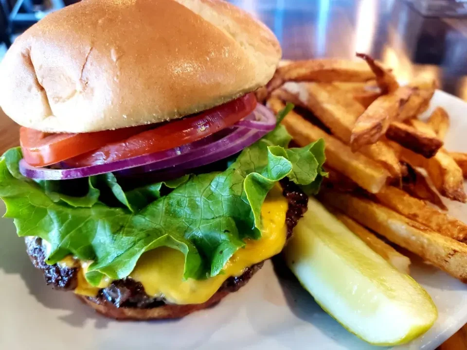 Cheeseburger, hand-cut fries, and pickle spear on a white plate.