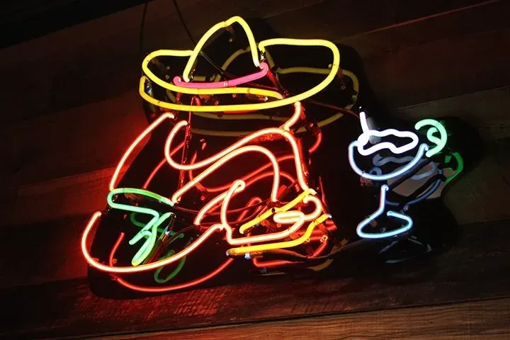 Neon signs of a sombrero figure and cocktail on dark background.