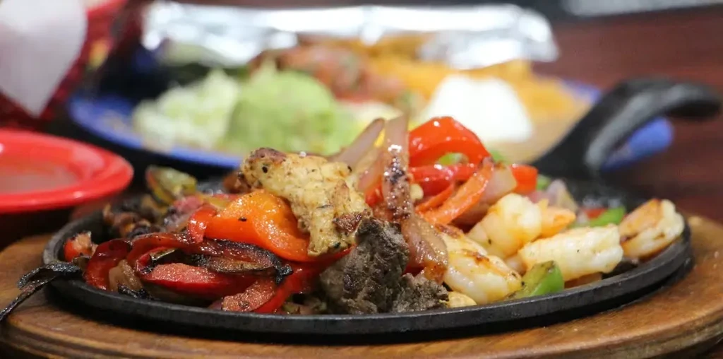 Sizzling chicken, beef, shrimp fajitas with vegetables in a skillet.