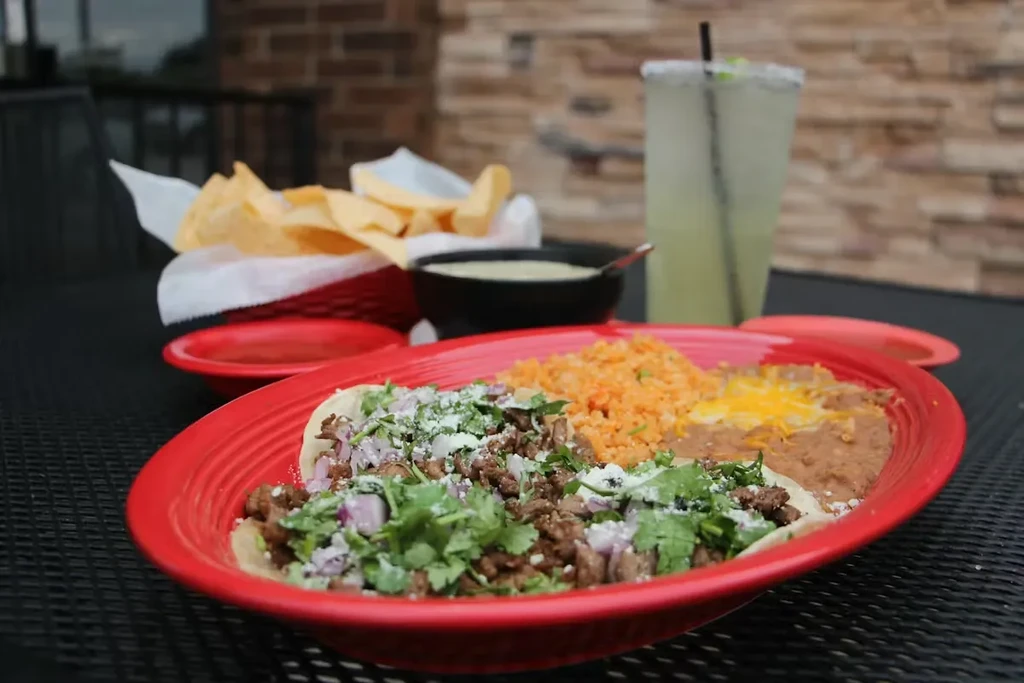 Ground beef tacos, rice, beans, and margarita on an outdoor table.