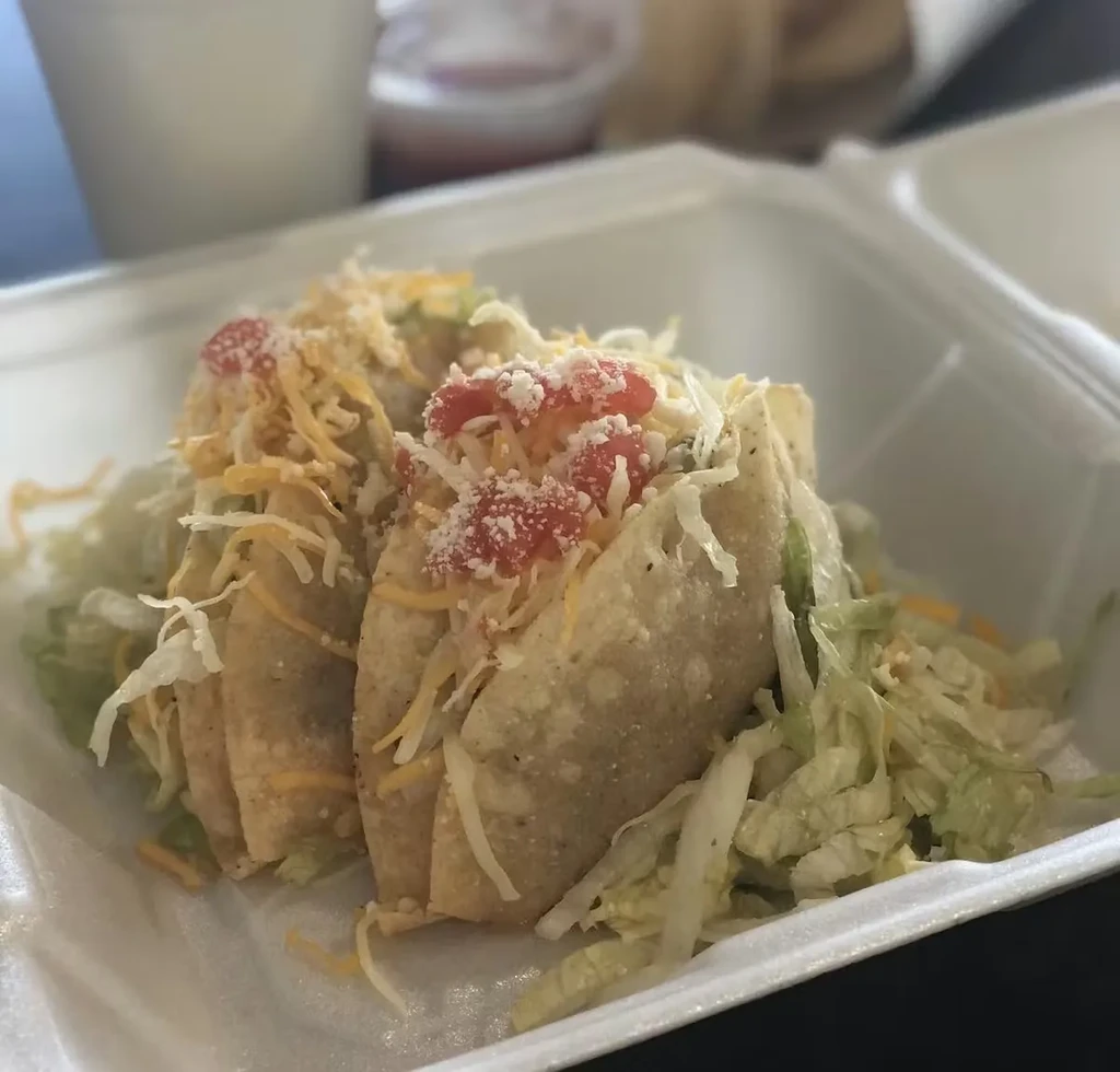 Three crispy tacos with lettuce, cheese, tomatoes, and cotija in takeout.